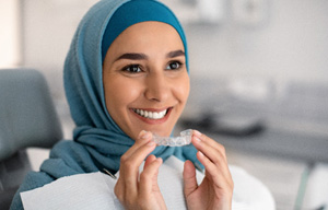 Woman in blue head wrap in dental chair holding Invisalign