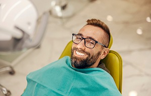 Man with glasses smiling while sitting in treatment chair
